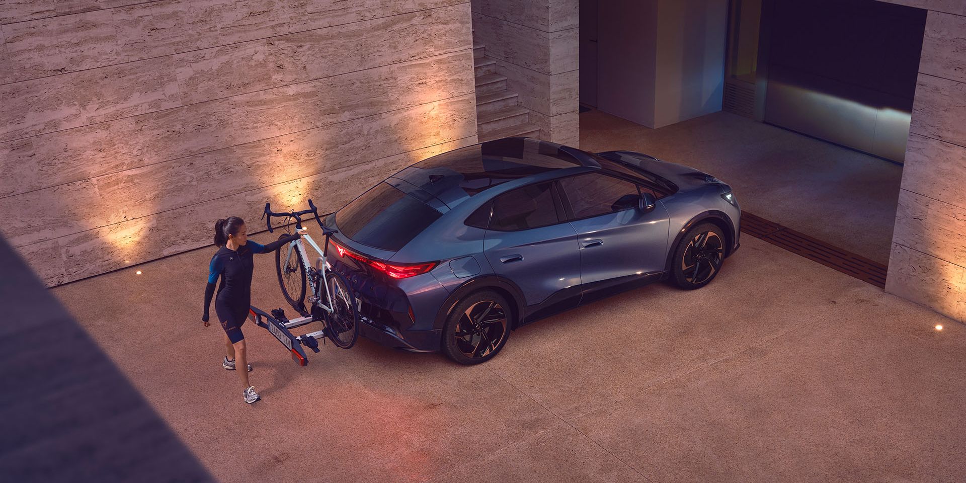Eine Frau greift zu einem Fahrrad, das auf dem Heckträger eines CUPRA Tavascan befestigt ist.