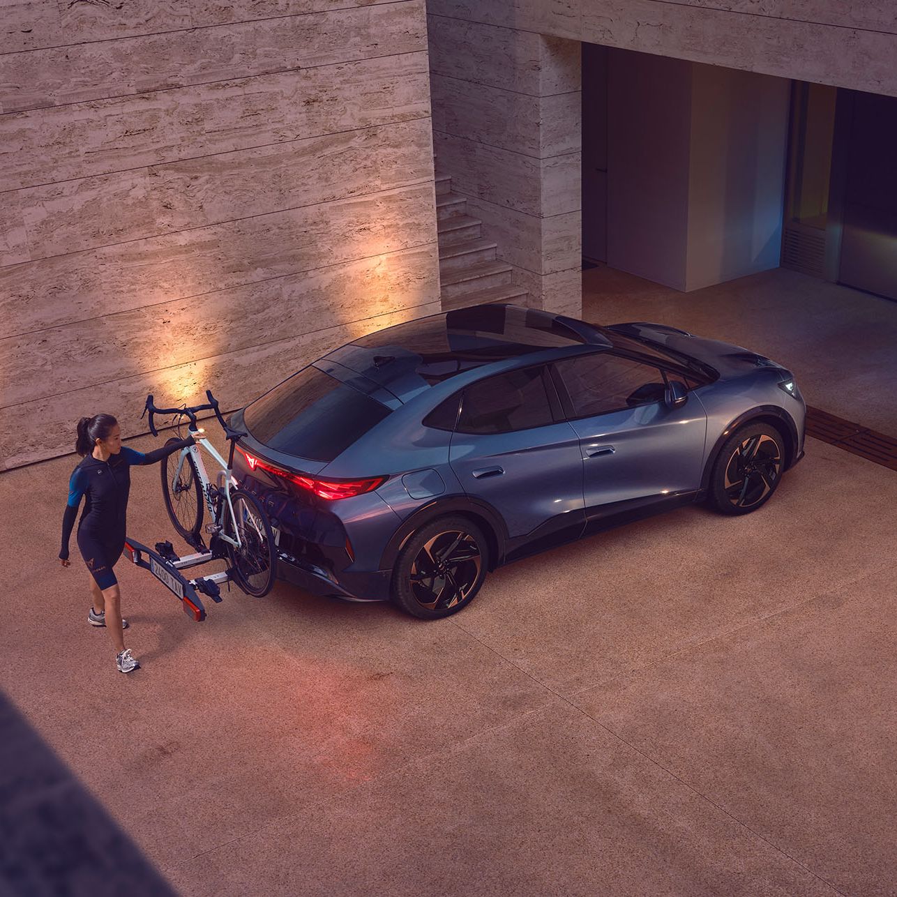 Eine Frau greift zu einem Fahrrad, das auf dem Heckträger eines CUPRA Tavascan befestigt ist.