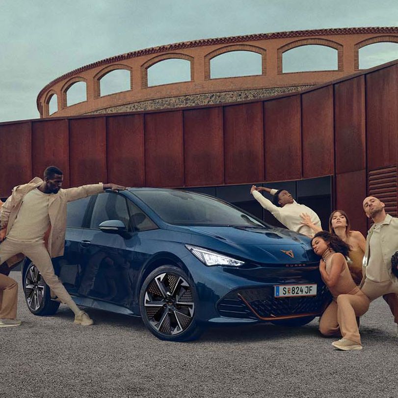 Ein blauer CUPRA Born steht auf einem Platz, mehrere Personen befinden sich links und rechts neben dem Fahrzeug.