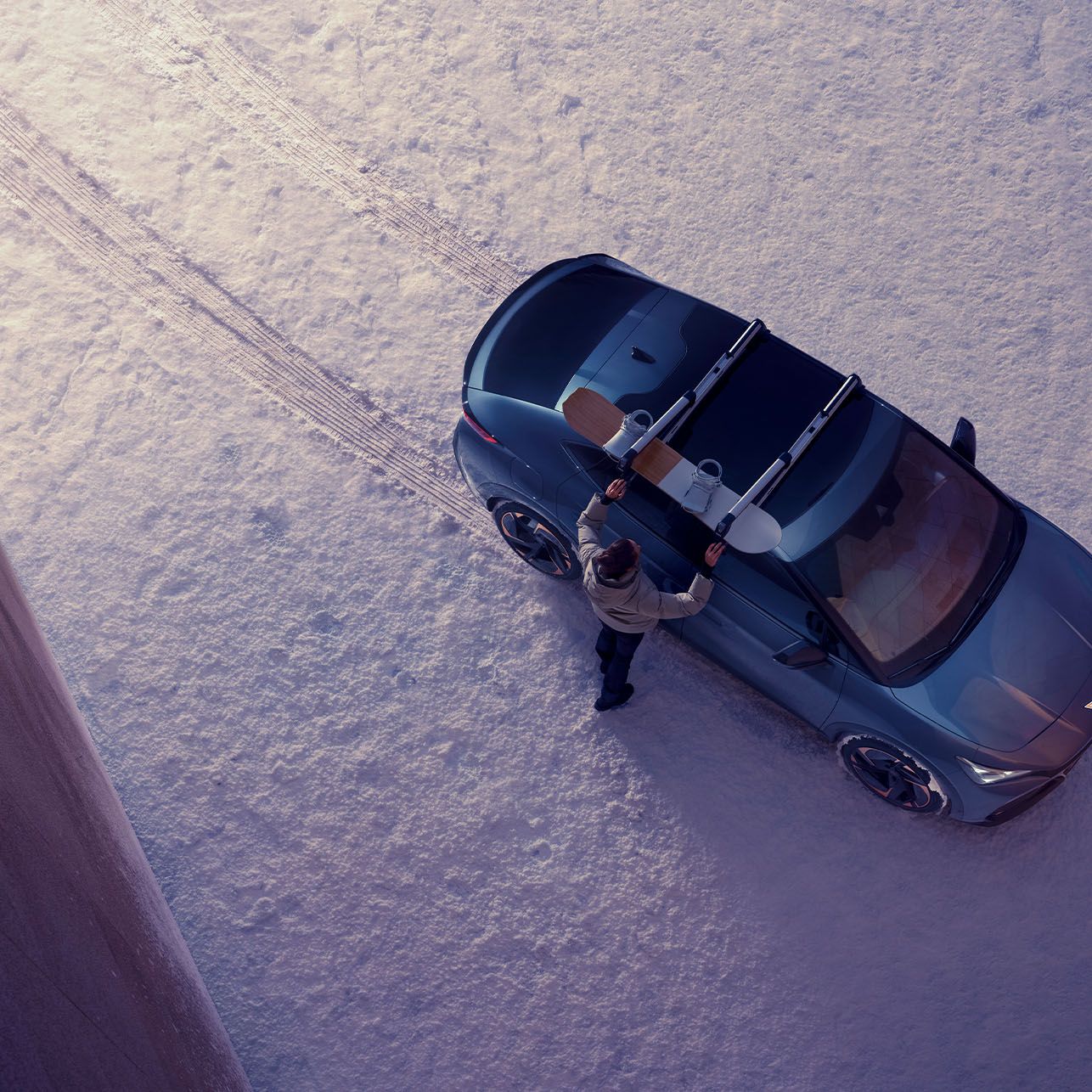 Eine Person befestigt ein Snowboard am Skiträger eines CUPRA Tavascan.