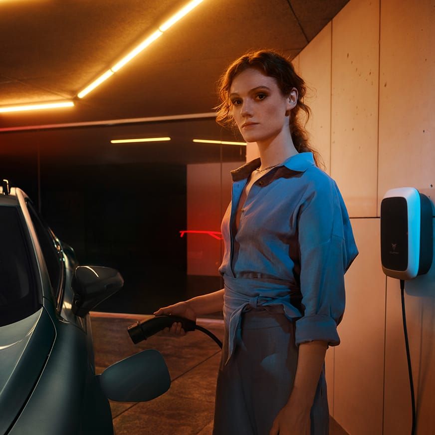 Eine Frau, die seitlich angelehnt neben einem CUPRA steht 