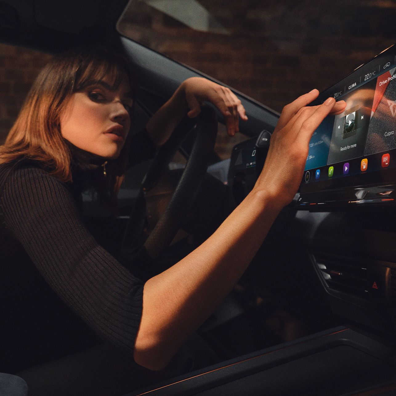 Eine Frau sitzt in einem CUPRA Born und bedient das Infotainment Display.
